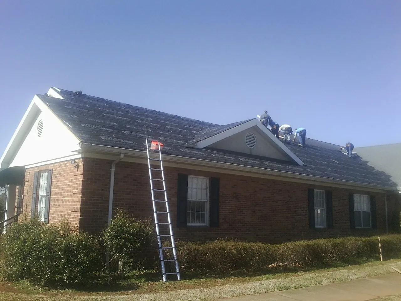 Crew tearing shingles off a brick ranch roof with a ladder set — Metal Roof Repair work by our crew in Reading